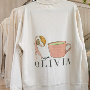 White sweatshirt on a hanger featuring a pink coffee cup illustration and the text OLIVIA beneath it.
