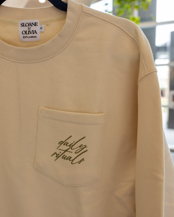 Beige sweatshirt on a hanger with a Sloane & Olivia label and a front pocket visible.